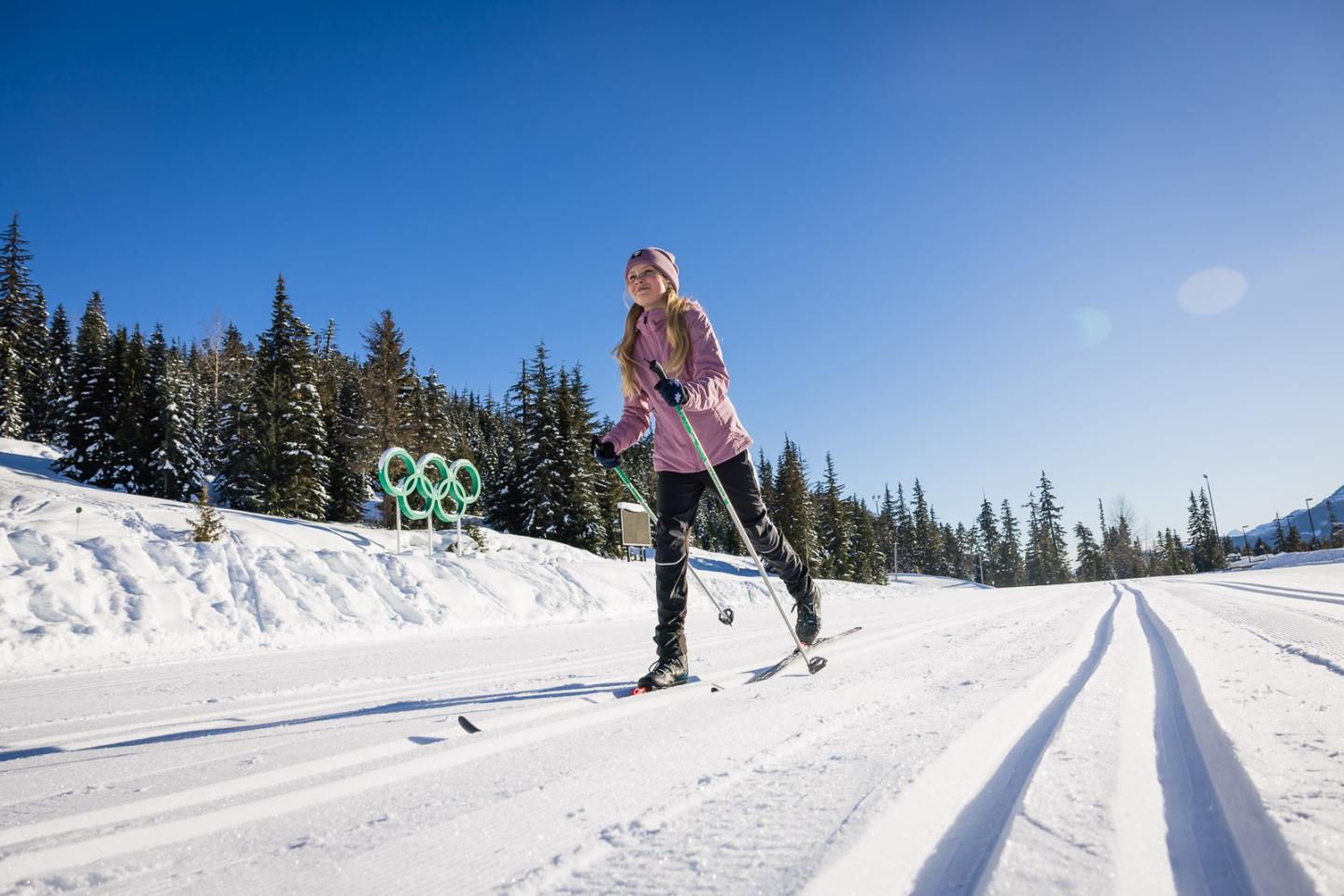 Cross-country skier in a snowy forest, under a clear blue sky.